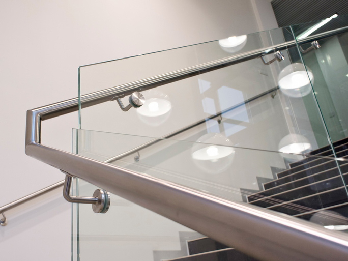 Barandal de vidrio templado en escalera interior con anclajes de acero inoxidable y pasamanos inoxidable