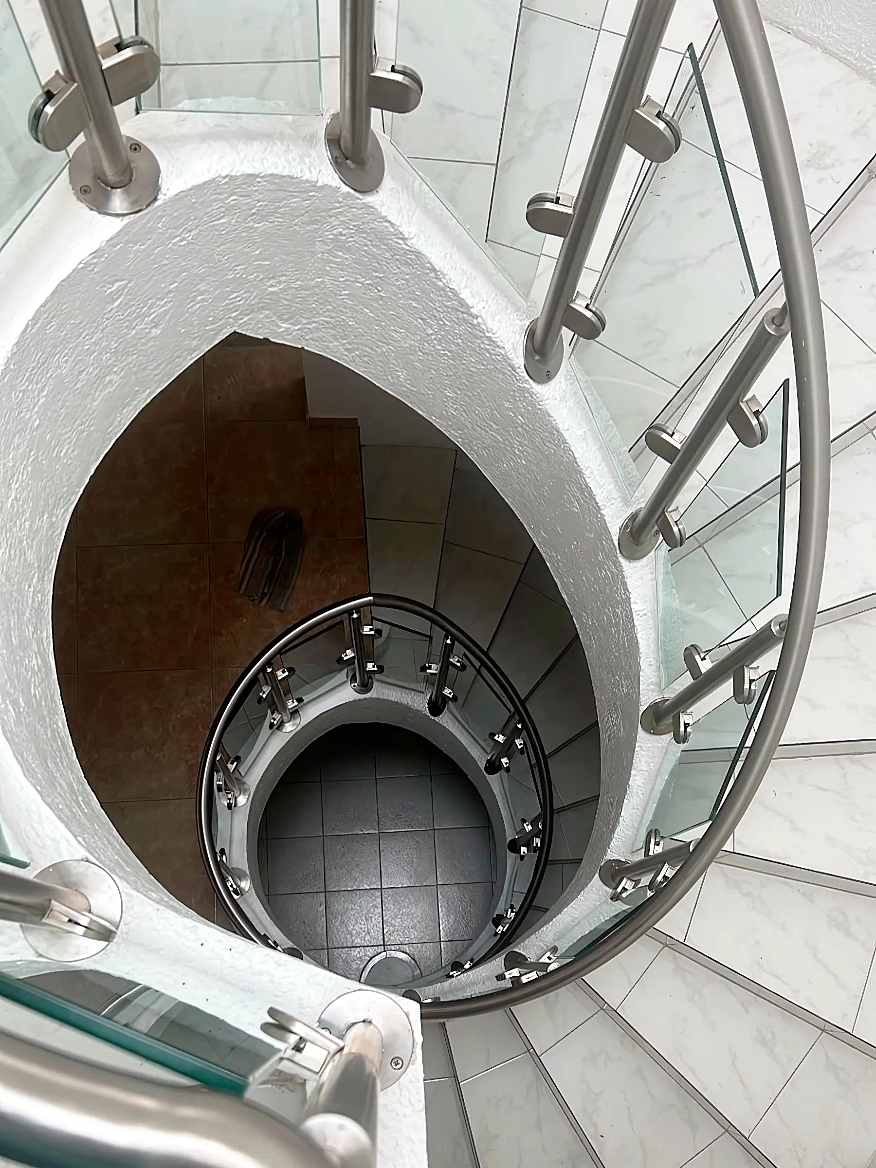 Barandal de vidrio templado y acero rodeando en escalera circular interior